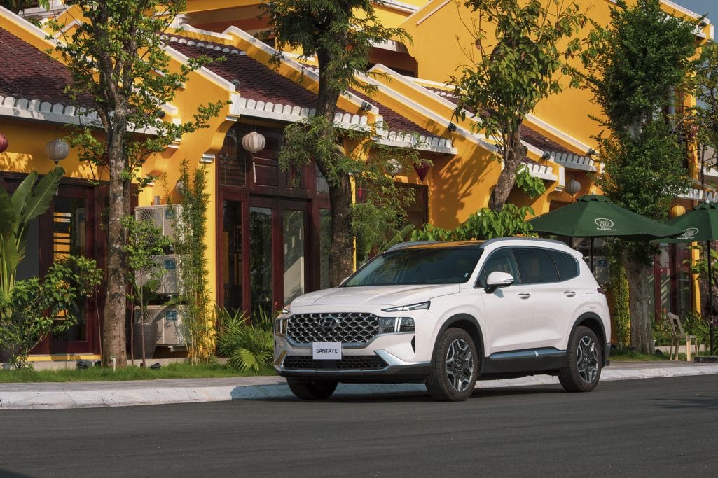 Hình ảnh xe ô tô Hyundai SantaFe Hybrid màu trắng đang di chuyển trên đường, thể hiện thiết kế hiện đại và thân thiện môi trường.