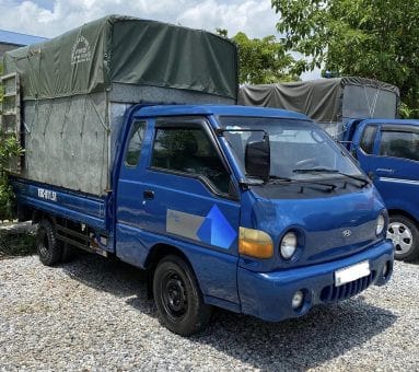 Hình ảnh xe tải Hyundai H100 1 tấn đời 2003 với thùng bạt màu xanh, vẫn còn hoạt động tốt.