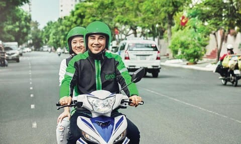 Khách hàng đặt xe Grab qua điện thoại và tài xế GrabBike đang chờ, nhấn mạnh tầm quan trọng của việc hiểu rõ giá cước khi sử dụng dịch vụ.