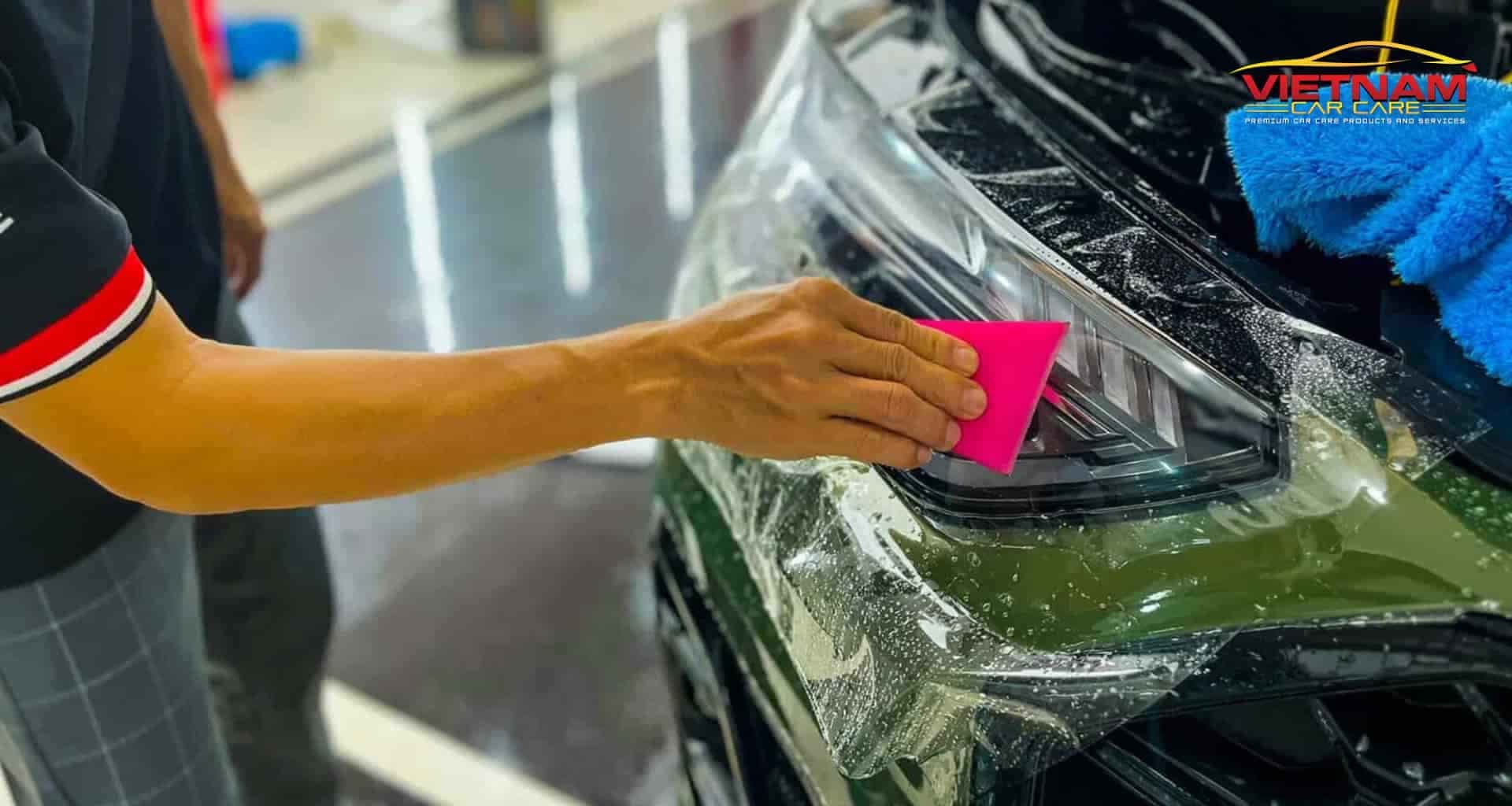 Kỹ thuật viên đang dán phim PPF bảo vệ sơn xe hơi màu trắng, đảm bảo chống trầy xước.