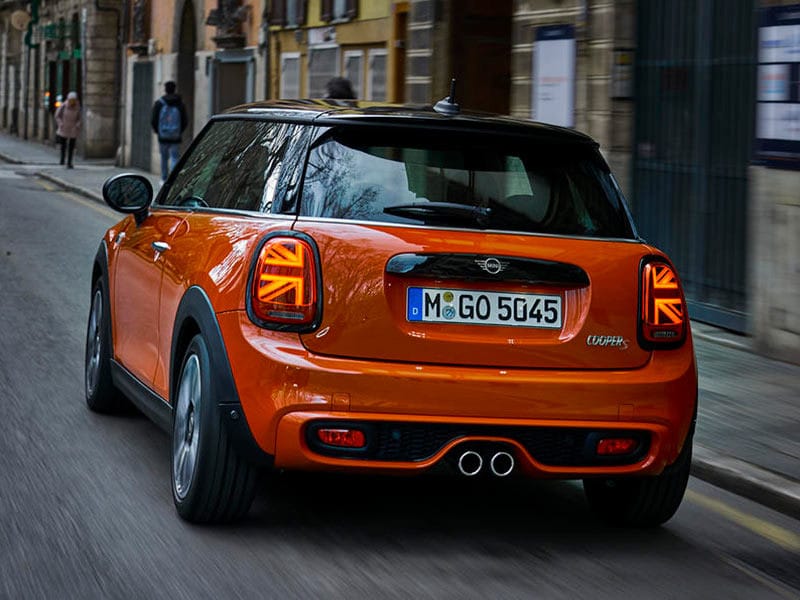 Mini Cooper màu xanh lá cây với mái màu trắng, thiết kế cổ điển và thể thao, đậu trên một con đường lát đá