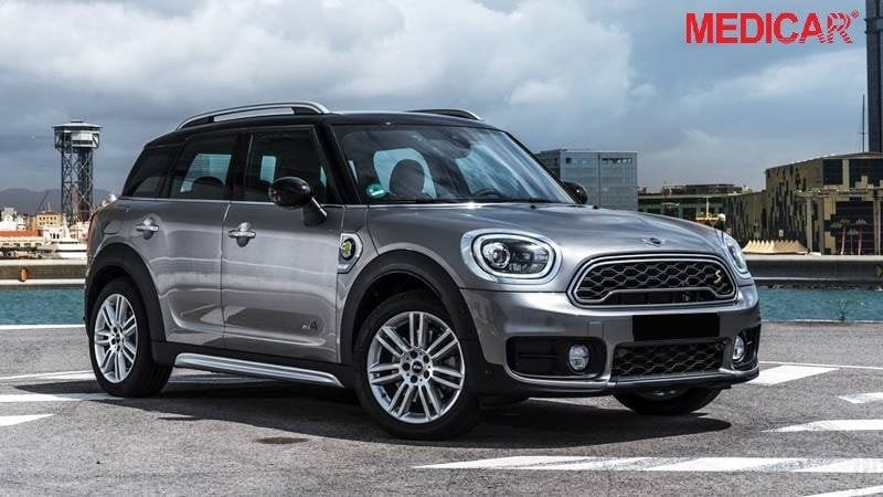 Một chiếc Mini Countryman màu xanh đang đỗ trên đường đất với cảnh núi non phía sau