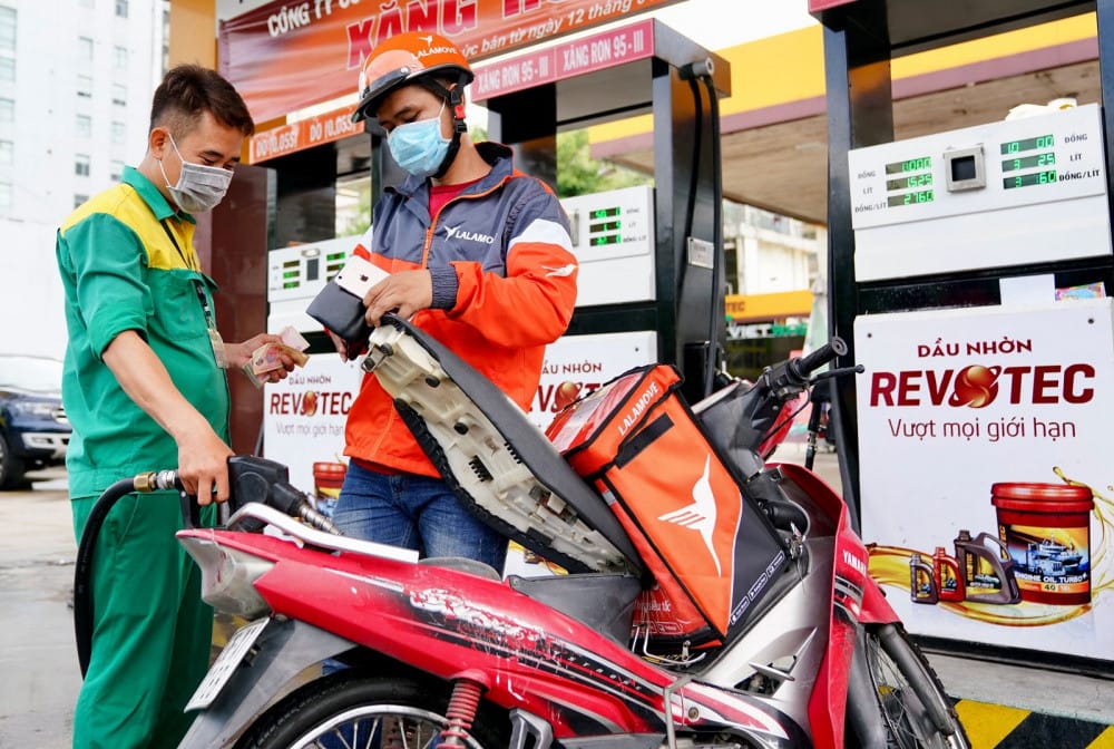 Một người đang đổ xăng vào chiếc xe máy tay ga tại trạm xăng với các loại xăng khác nhau