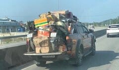 Một xe tải van chở hàng hóa cồng kềnh trên nóc thùng xe, di chuyển trên đường