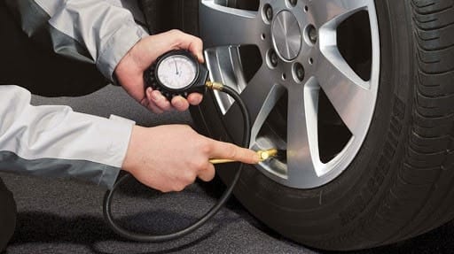 Người lái xe kiểm tra áp suất lốp xe 7 chỗ bằng đồng hồ đo áp suất