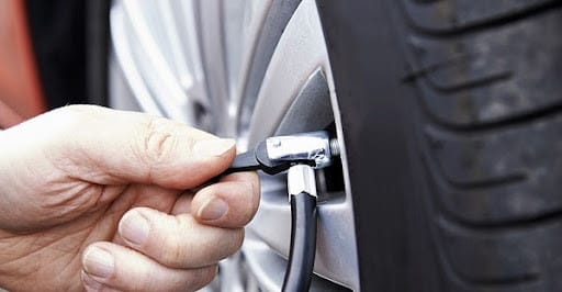 Người lái xe kiểm tra lốp ô tô trước khi sử dụng máy bơm xe mini để đảm bảo an toàn trên đường