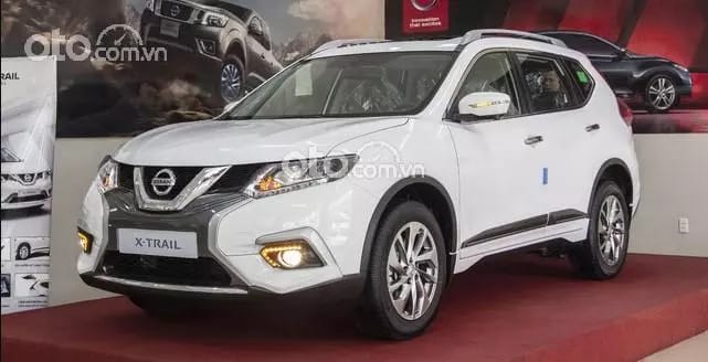Nissan X-Trail 2021 màu trắng bạc đỗ cạnh hàng cây xanh mướt, thể hiện sự linh hoạt của một chiếc crossover.