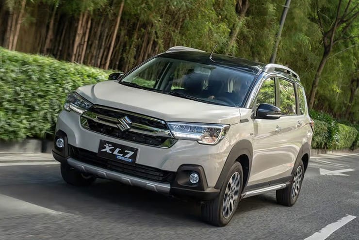 Ô tô 7 chỗ giá rẻ Suzuki XL7 Hybrid màu trắng di chuyển trên đường phố, tượng trưng cho sự tiết kiệm nhiên liệu.