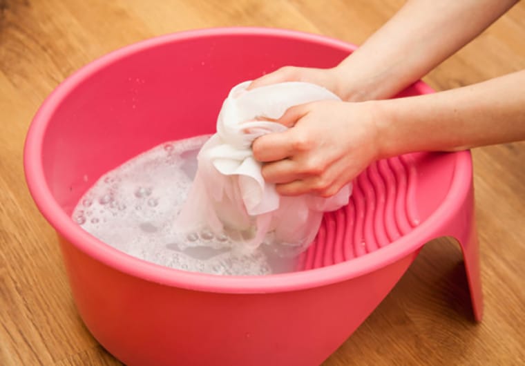 Phụ nữ đang giặt áo màu bị dính dầu nhớt bằng tay
