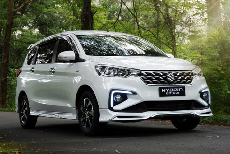 Suzuki Ertiga Hybrid màu trắng đỗ cạnh hàng cây xanh