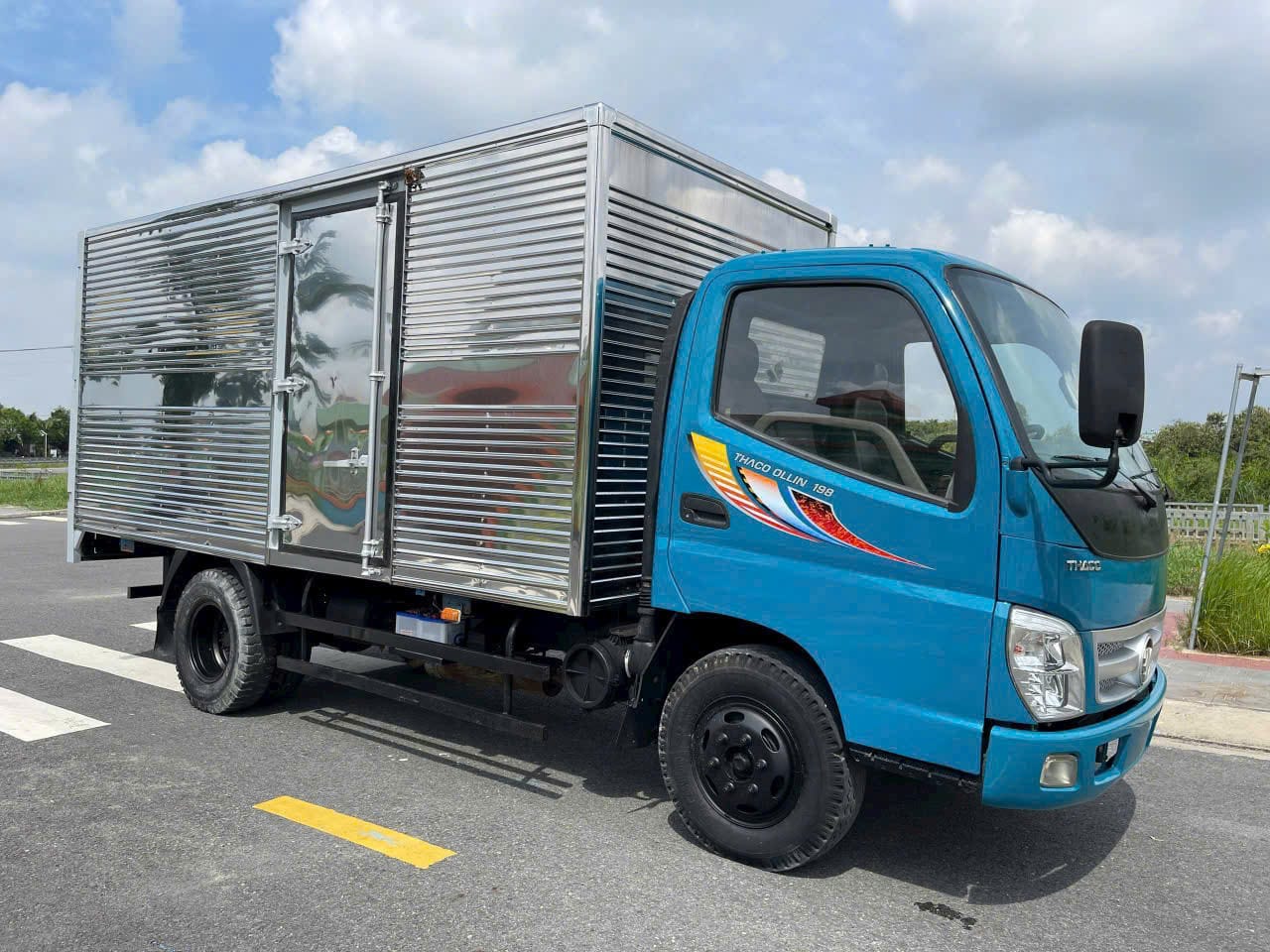 xe tải Thaco Ollin 2 tấn cũ màu xanh dương, thùng mui bạt, đang vận hành trên đường